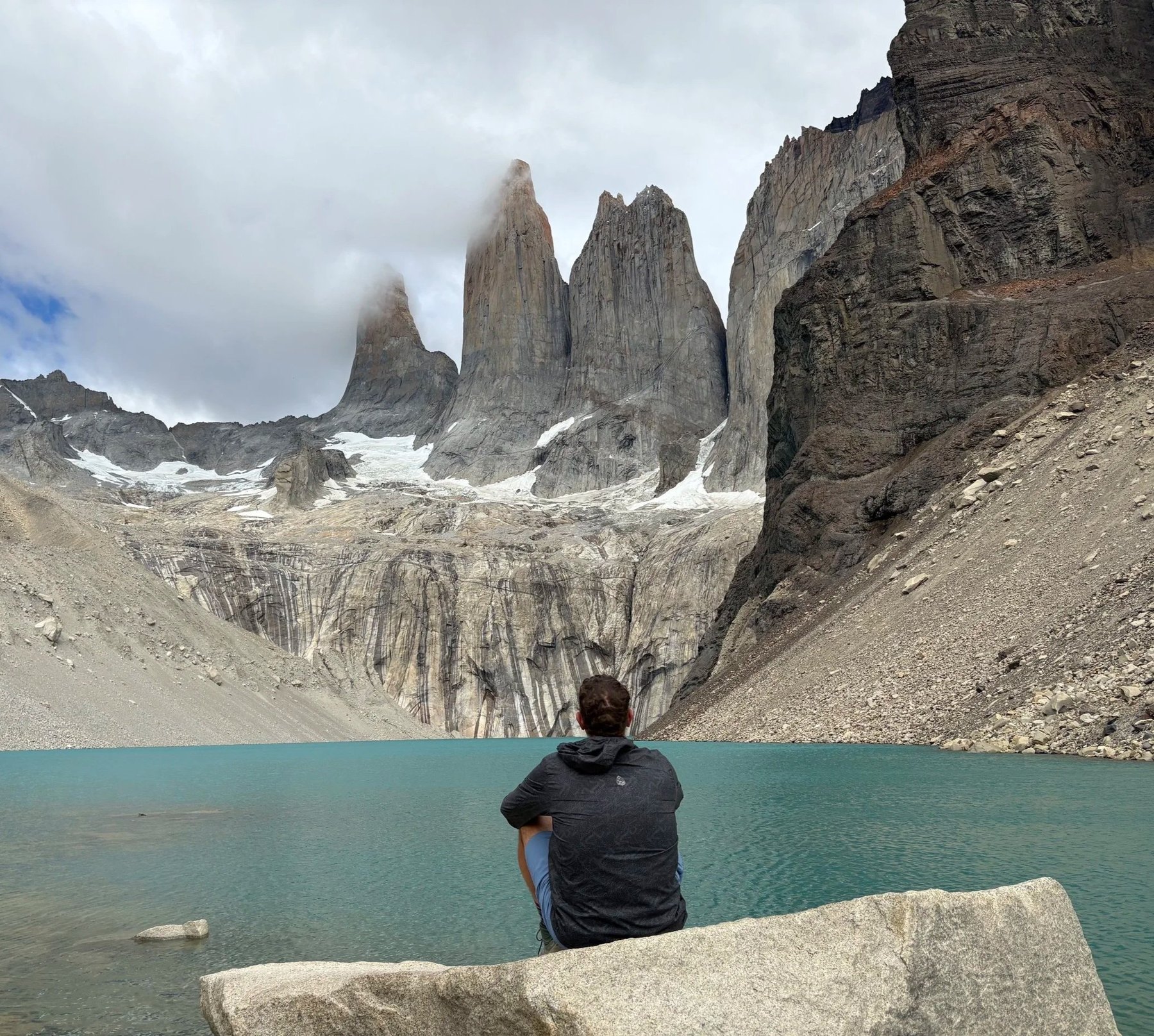 A person looking out across a turquoise lake toward mountain peaks